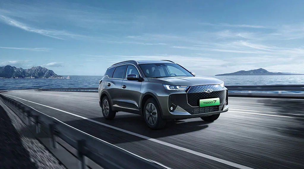 Chery Tiggo 7 w kolorze grafitowym, ujęcie przód-bok podczas jazdy nad wybrzeżem, w tle morze i skały