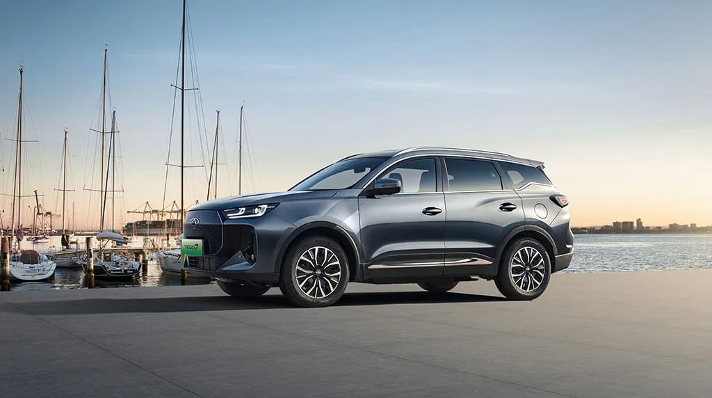 Chery Tiggo 7 w kolorze szarym, widok z boku, w tle marina z jachtami o zachodzie słońca