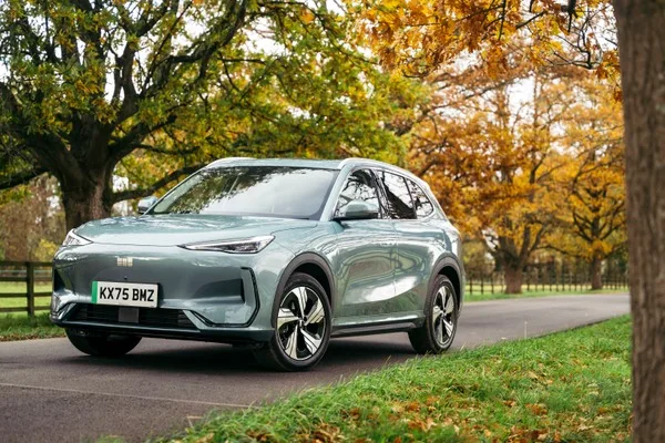 Geely EX5 w kolorze szarym, widok od przodu w 3/4, na tle jesiennej alei drzew