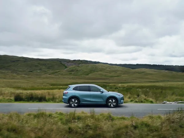 Geely EX5 Max w kolorze jadeitowej zieleni, widok z boku w ruchu na wiejskiej drodze wśród wzgórz