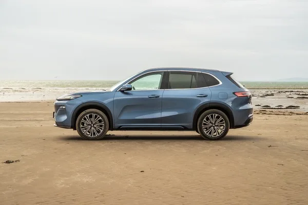 Geely Starray EM-i w kolorze niebieskim, widok z boku na piaszczystej plaży z morzem w tle