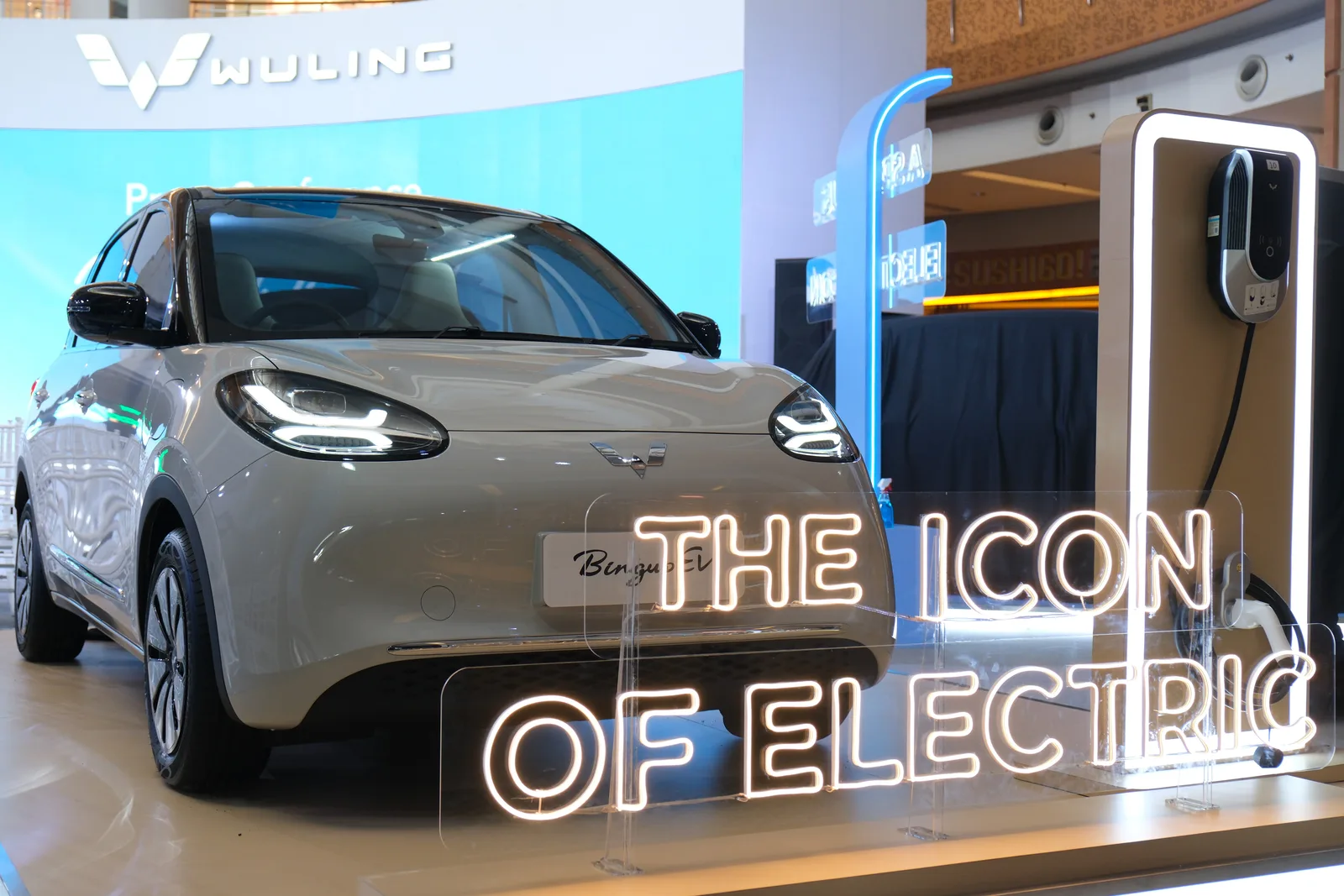 Wuling Bingo, zblizenie na przod nadwozia w kolorze szarobezowym, w tle stacja ladowania i neonowy napis The Icon of Electric